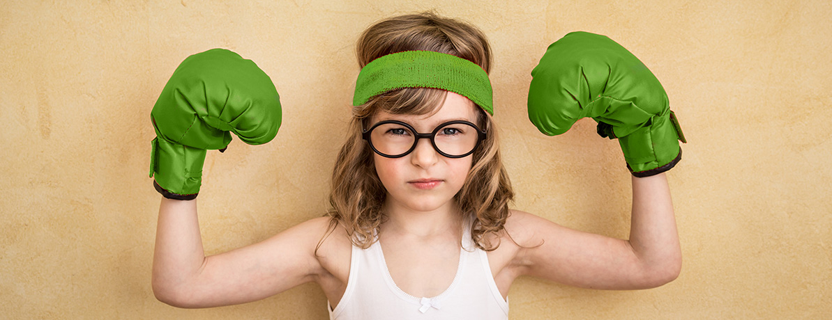 A young girl wearing green boxing gloves flexing her arms