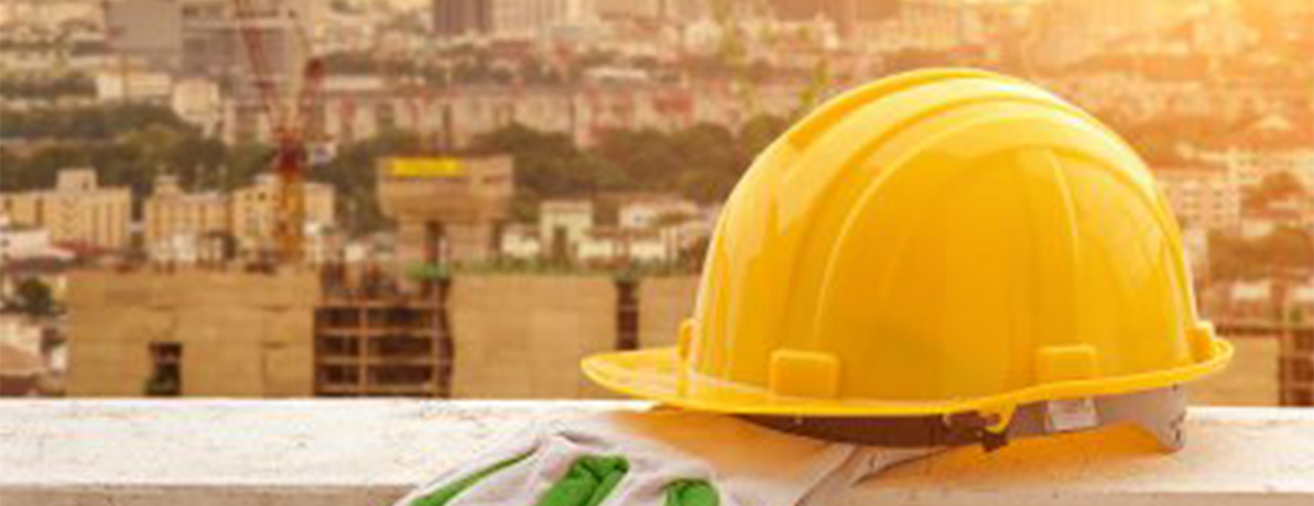 Un casque de chantier jaune posé sur une corniche avec un chantier en arrière-plan